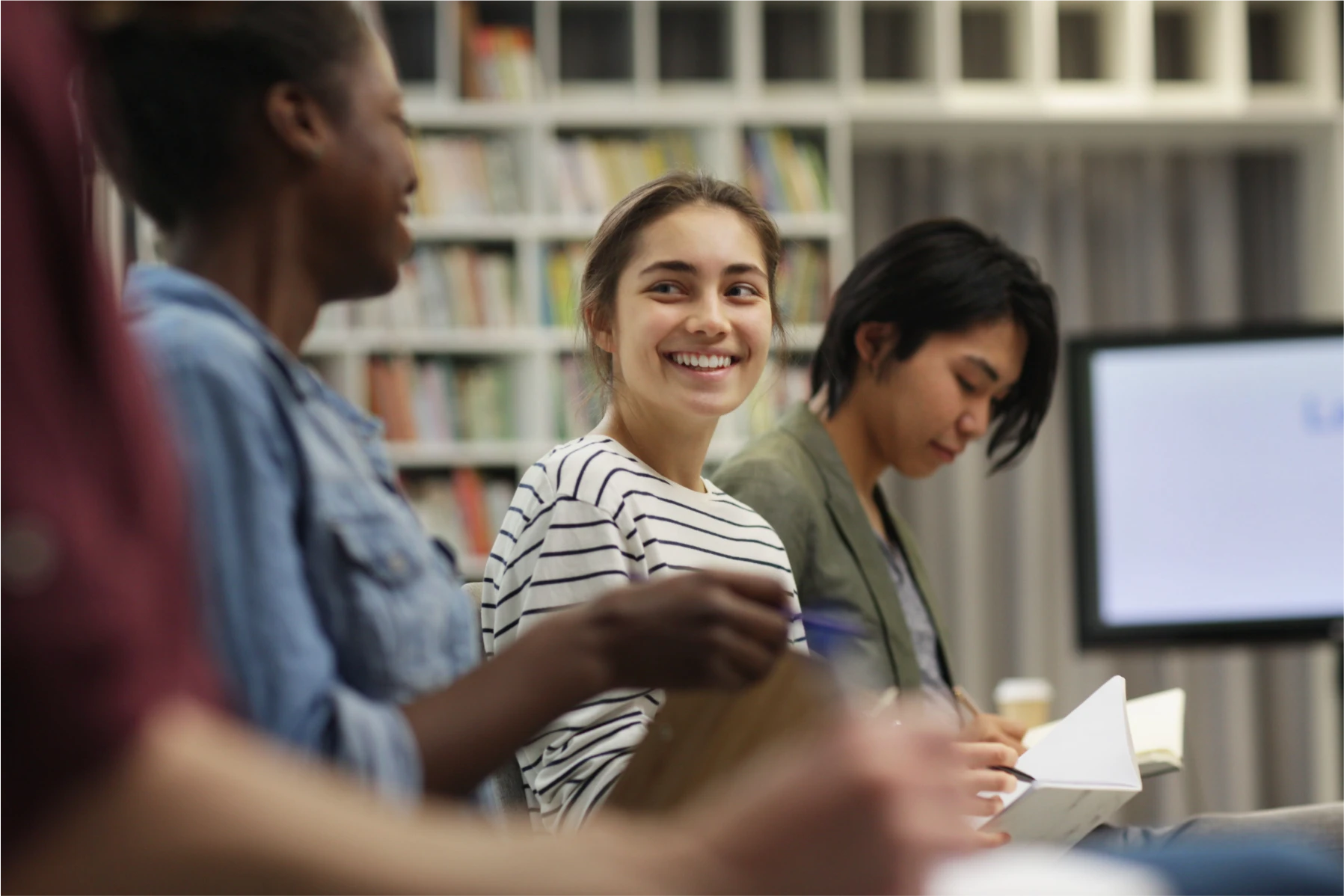 Smiling student in a study group with books and notes.
