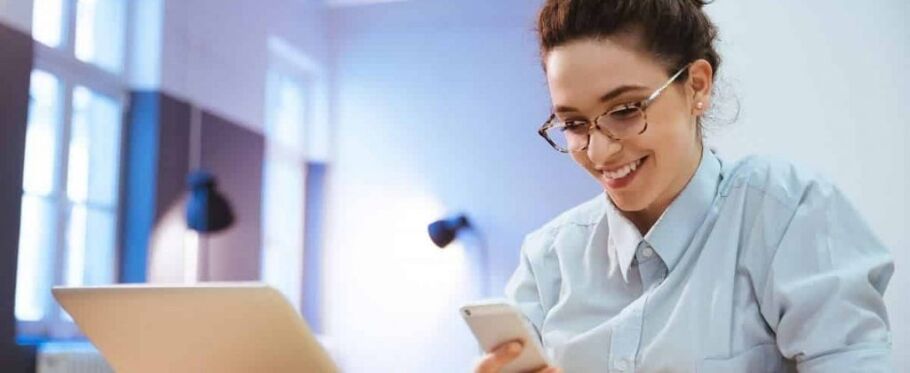 Smiling student checks phone near laptop, possibly about college applications.