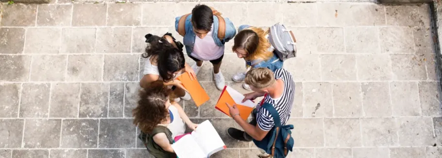 Students collaborate, reviewing college applications and essays together outdoors.