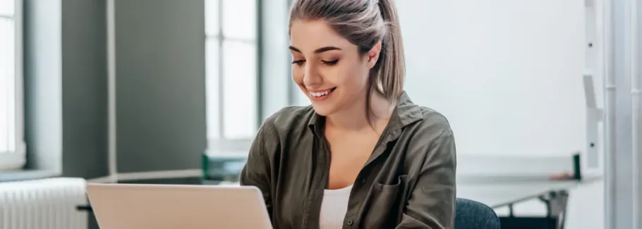 Smiling student works on laptop, preparing for college applications.
