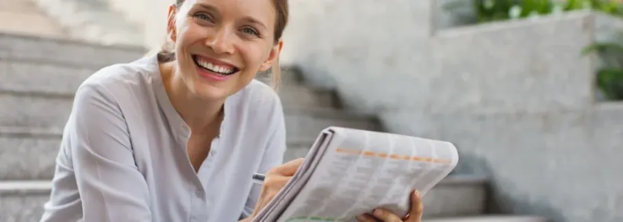Smiling student reviews college options in a newspaper.