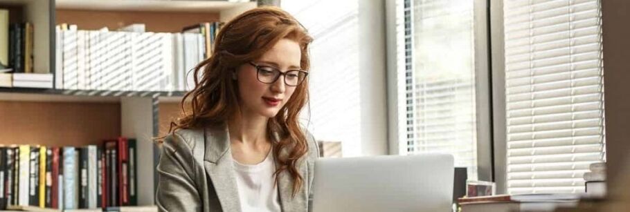 Student researches college options using a laptop with books and natural light.