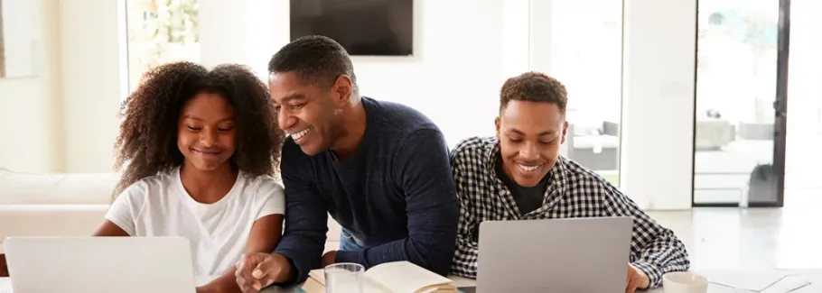 African-American father standing between a boy and a girl with laptops, looking at the girl's laptop