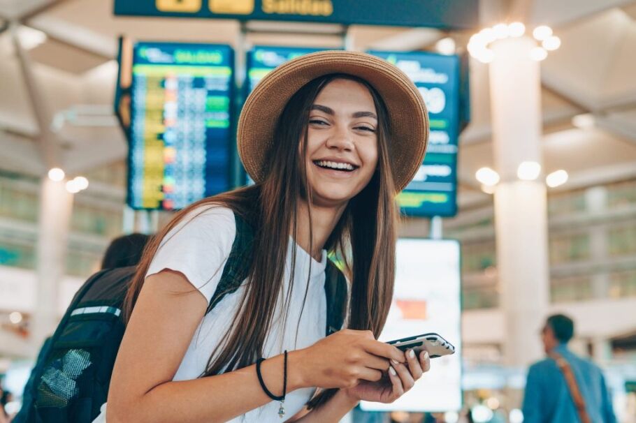 Smiling student traveler with backpack checks phone at airport.