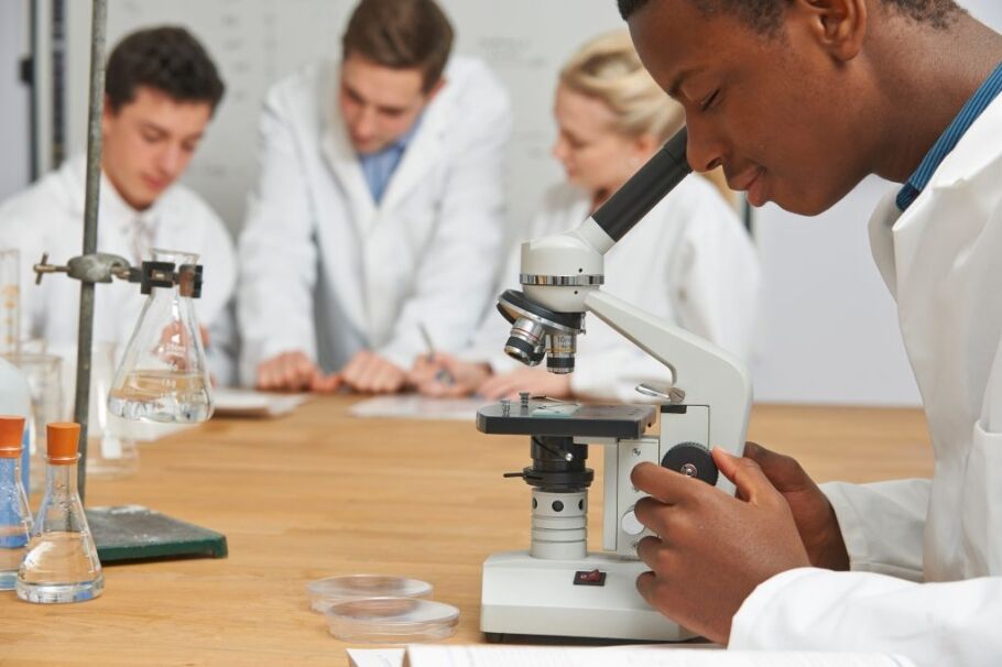 Students in lab coats using a microscope for science education.