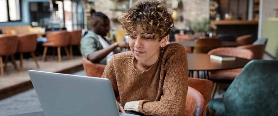 Student works on laptop in cafe, possibly researching college options.