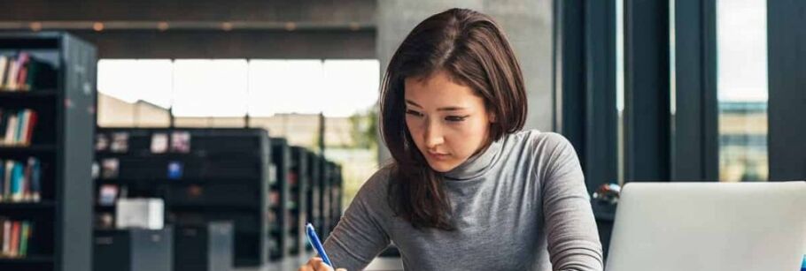 Student studying with laptop in library, focused on academic success.