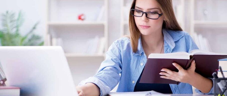 Student researches colleges using a laptop and book for admissions information.