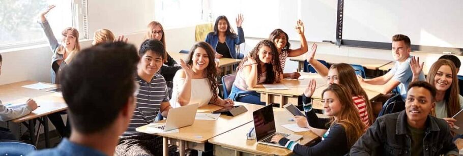 Enthusiastic students raise hands in a bright classroom, ready to learn.