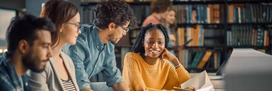 Students collaborate in a library, possibly discussing college applications or academic coursework.