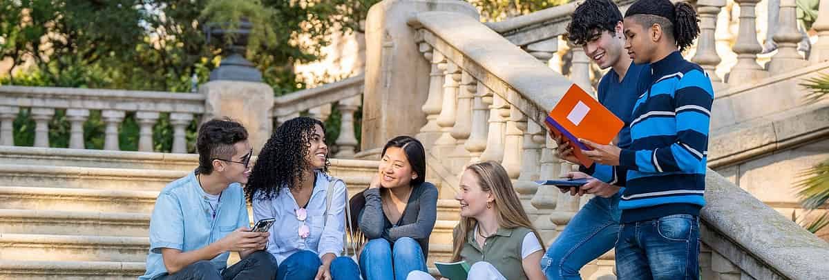 Diverse students studying together on stone steps, possibly on a college campus.