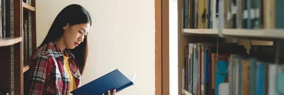 Student reading a book in a library, focused on academic success.