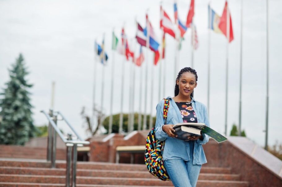 Student with books on campus with international flags, representing global education.