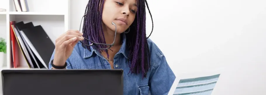 Student reviews college application data with laptop and glasses.