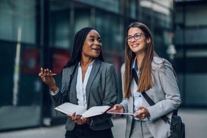 Two young professionals discuss college admissions strategies outdoors.