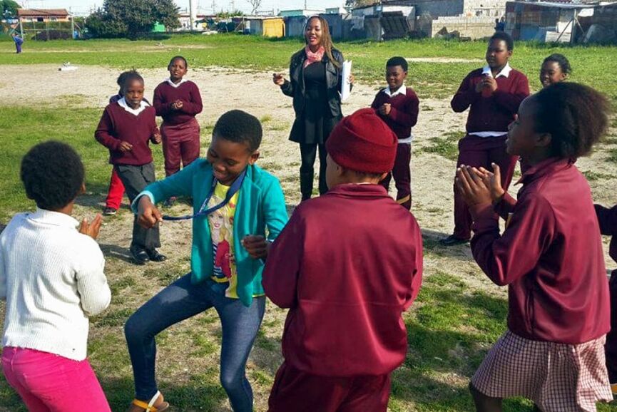Students playing a game outdoors with a teacher, fostering teamwork and learning.
