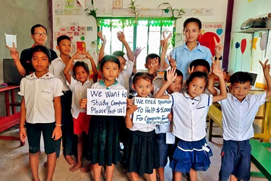 Students in classroom holding signs requesting computer study support.