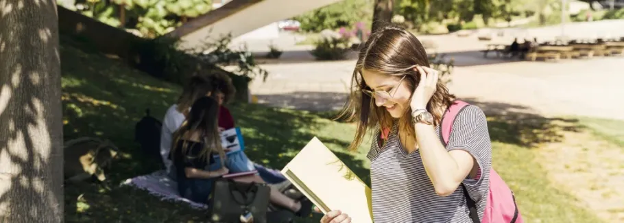 Graduate student with textbook and backpack walking across campus.