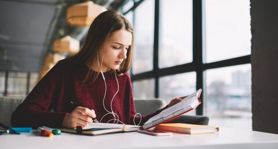 Student studying with headphones, taking notes for college applications.