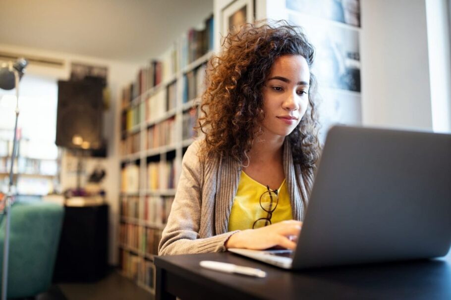 Student researches college options using laptop in library setting.