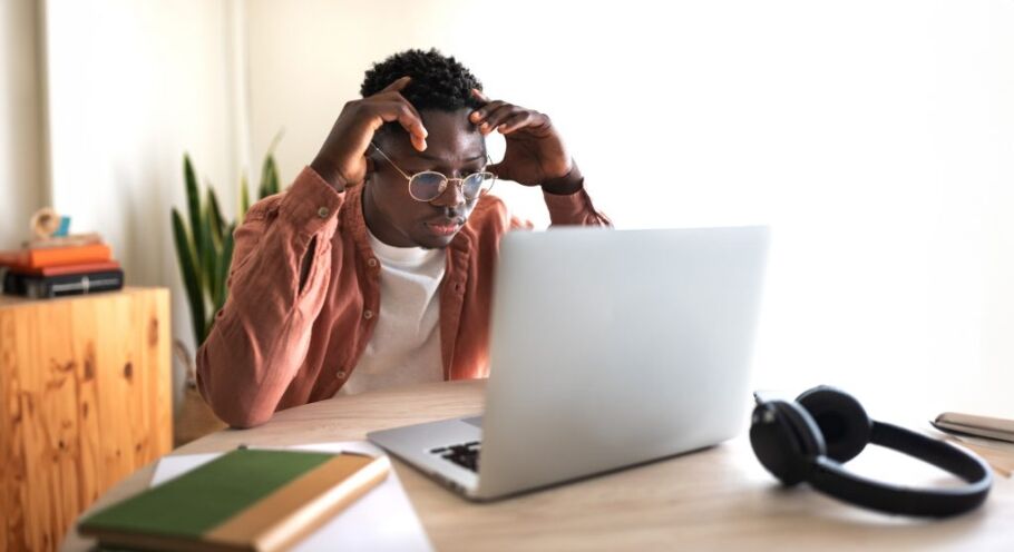 Stressed student with laptop, books, and headphones struggles with college application process.