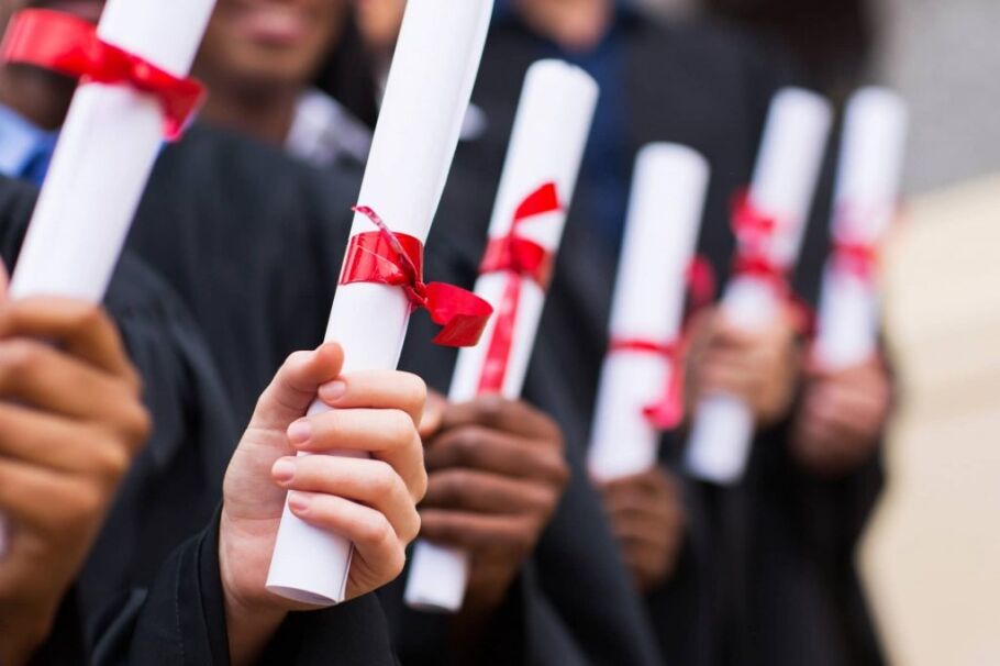 Graduates in gowns holding diplomas tied with red ribbons.