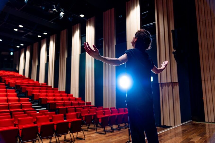 Student on stage with arms open, ready for college theater performance.