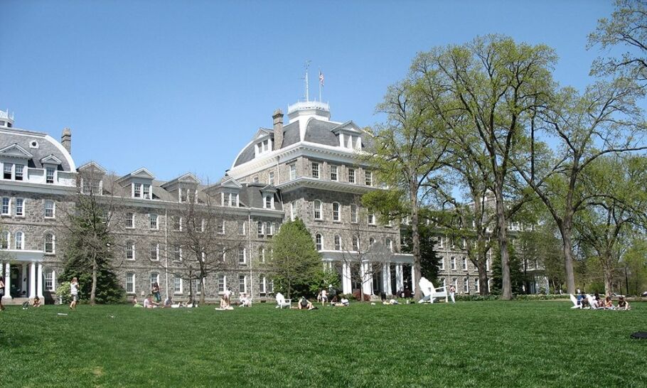 Students relax on the lawn of a traditional college campus building.