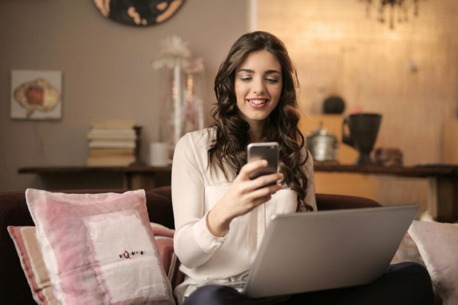 Student checks college application status on phone with laptop nearby.