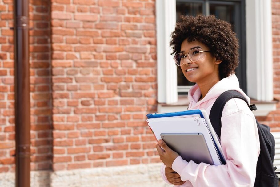 Smiling student with books and tablet looks toward a bright future.