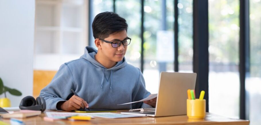 Student working on a laptop with a stylus and paper.
