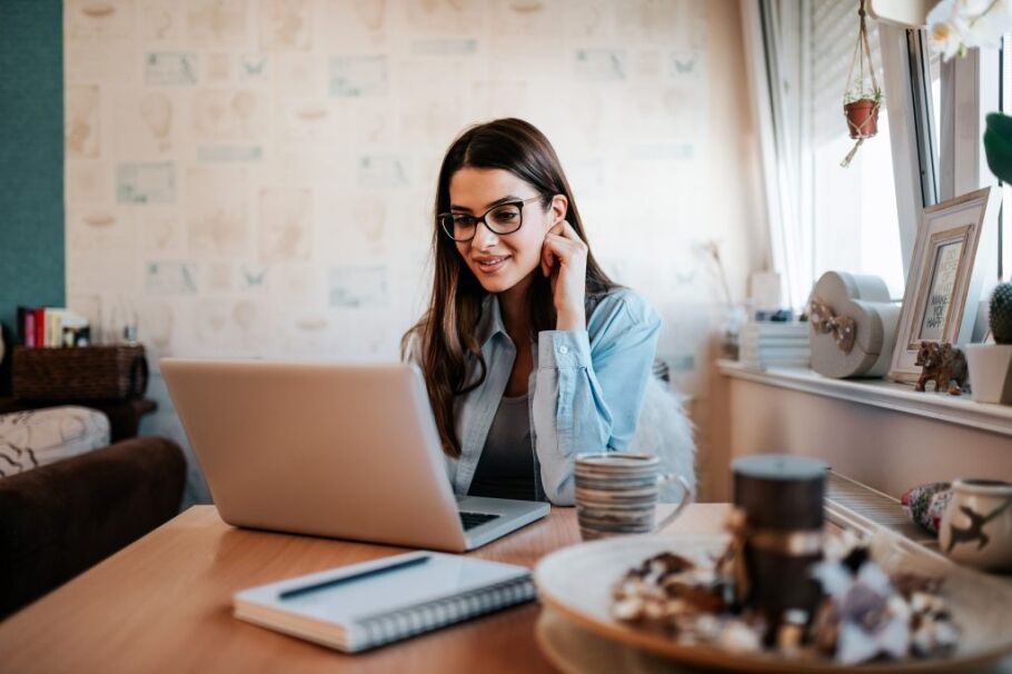 Student wearing glasses studies at laptop in a cozy home environment.