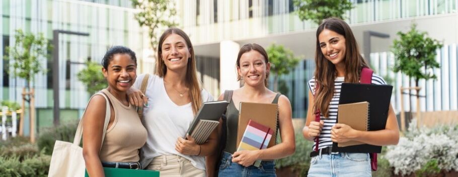Smiling students with books and folders on a college campus.